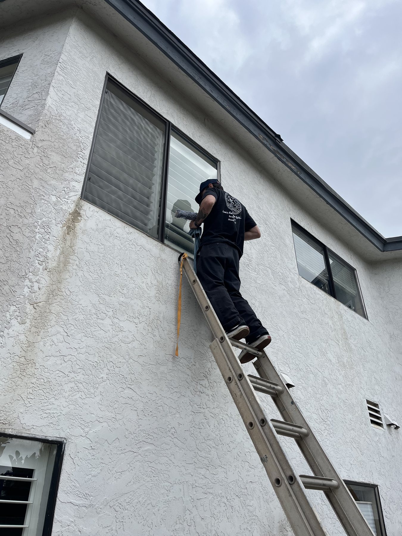 Waves technician cleaning a second-story window from a ladder