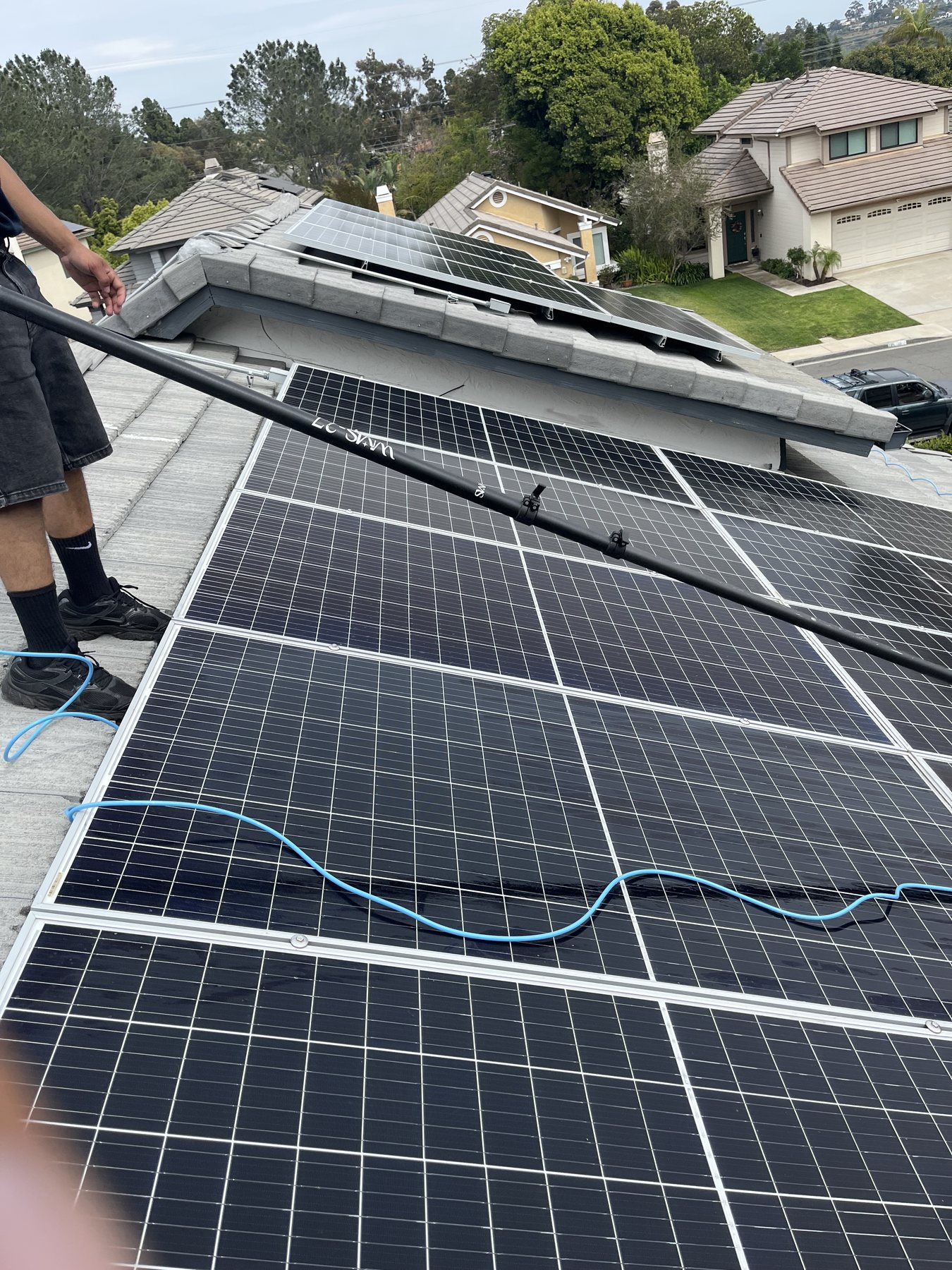 Waves technician cleaning solar panels with a deionized water-fed pole system